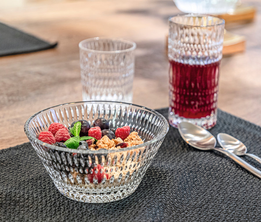 Eine mit Müsli und Früchten gefüllte Schale und ein Glas Getränk auf einem Tischset.