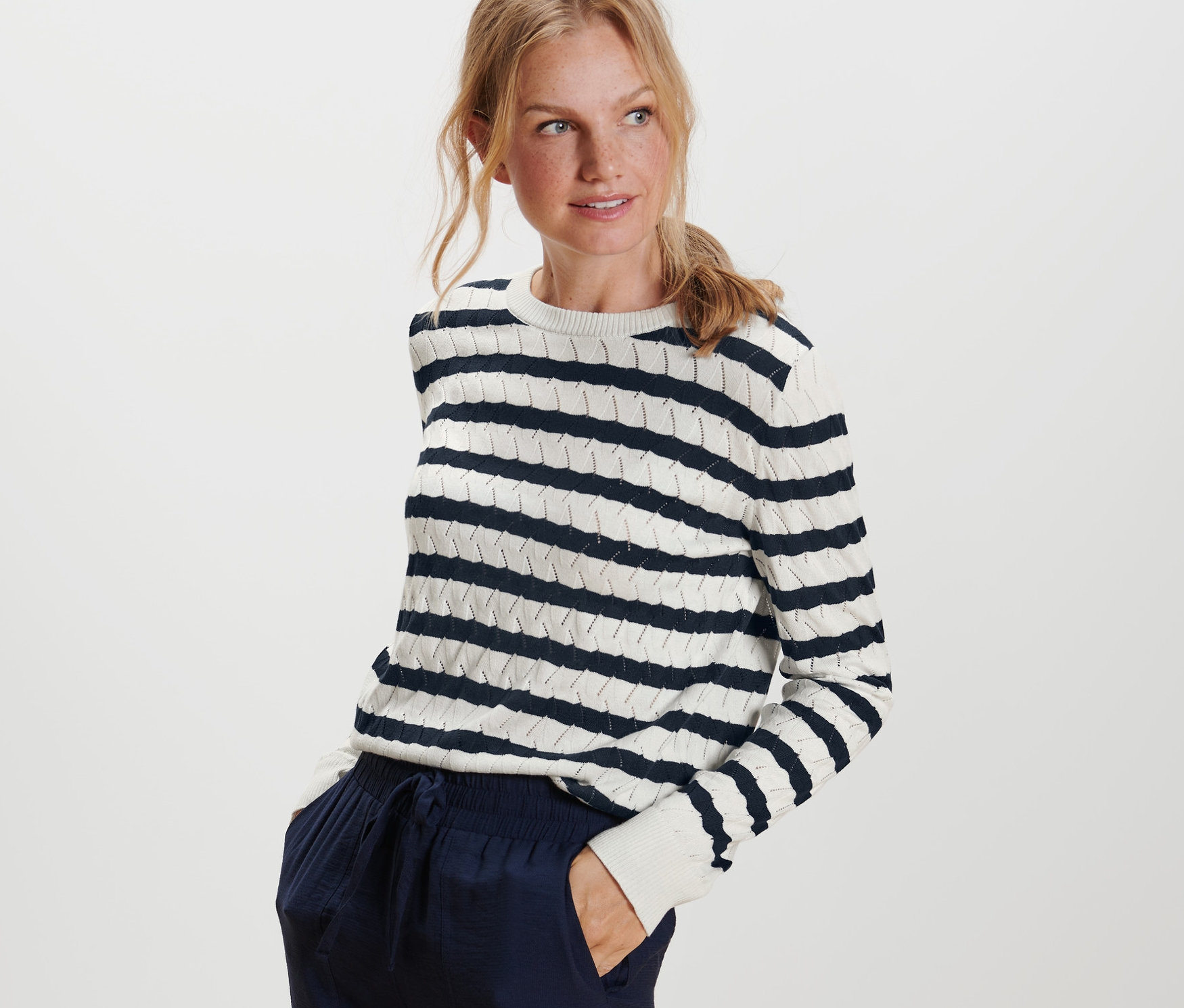 Blonde Frau posiert in einem gestreiften Strickpullover.