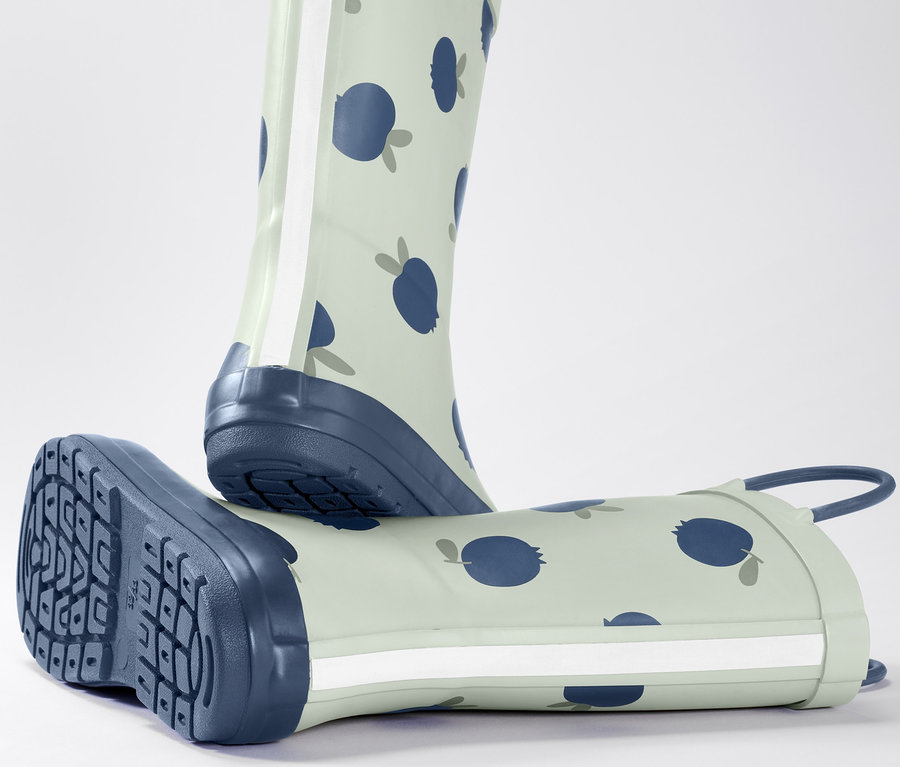 Ein Kleinkind-Regenstiefel mit Blaubeermuster steht, der andere liegt.