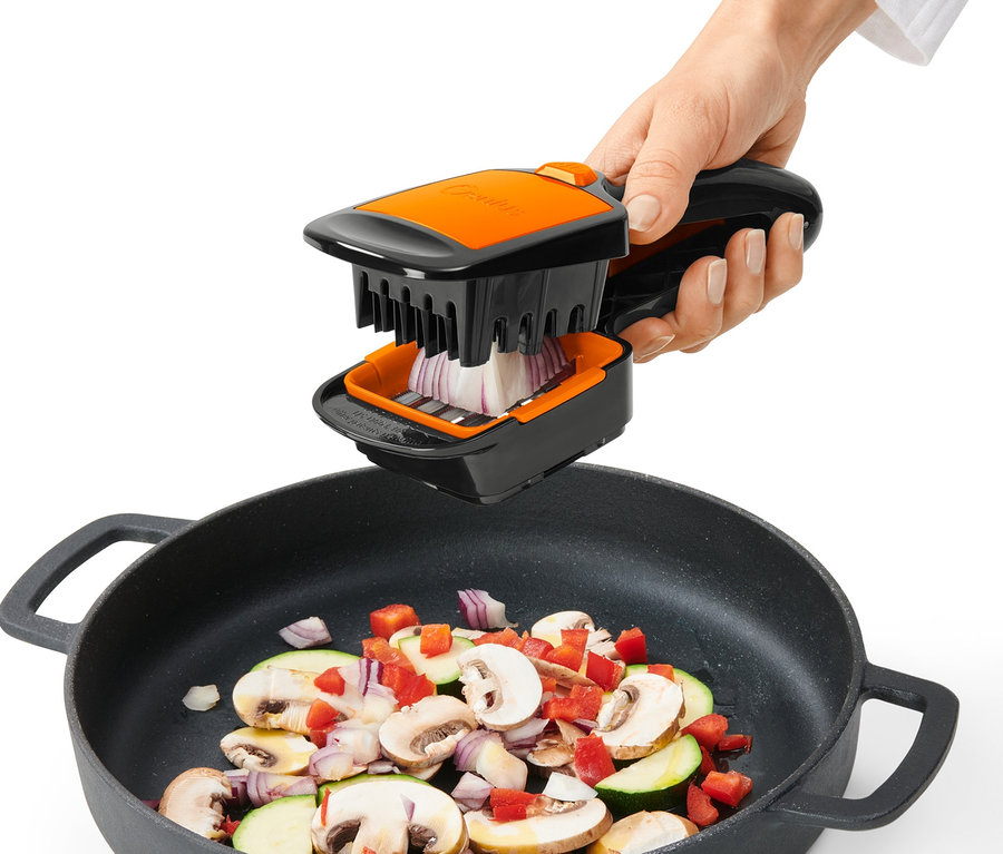 Eine Hand benutzt den Nicer Dicer Quick XXL, um Zwiebeln über einer Pfanne mit Gemüse zu schneiden.
