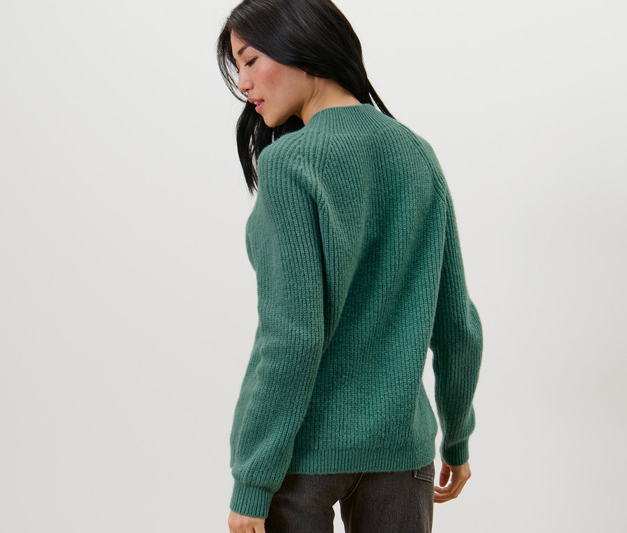 Frau von hinten trägt einen grünen Grobstrickpullover mit Stehkragen.