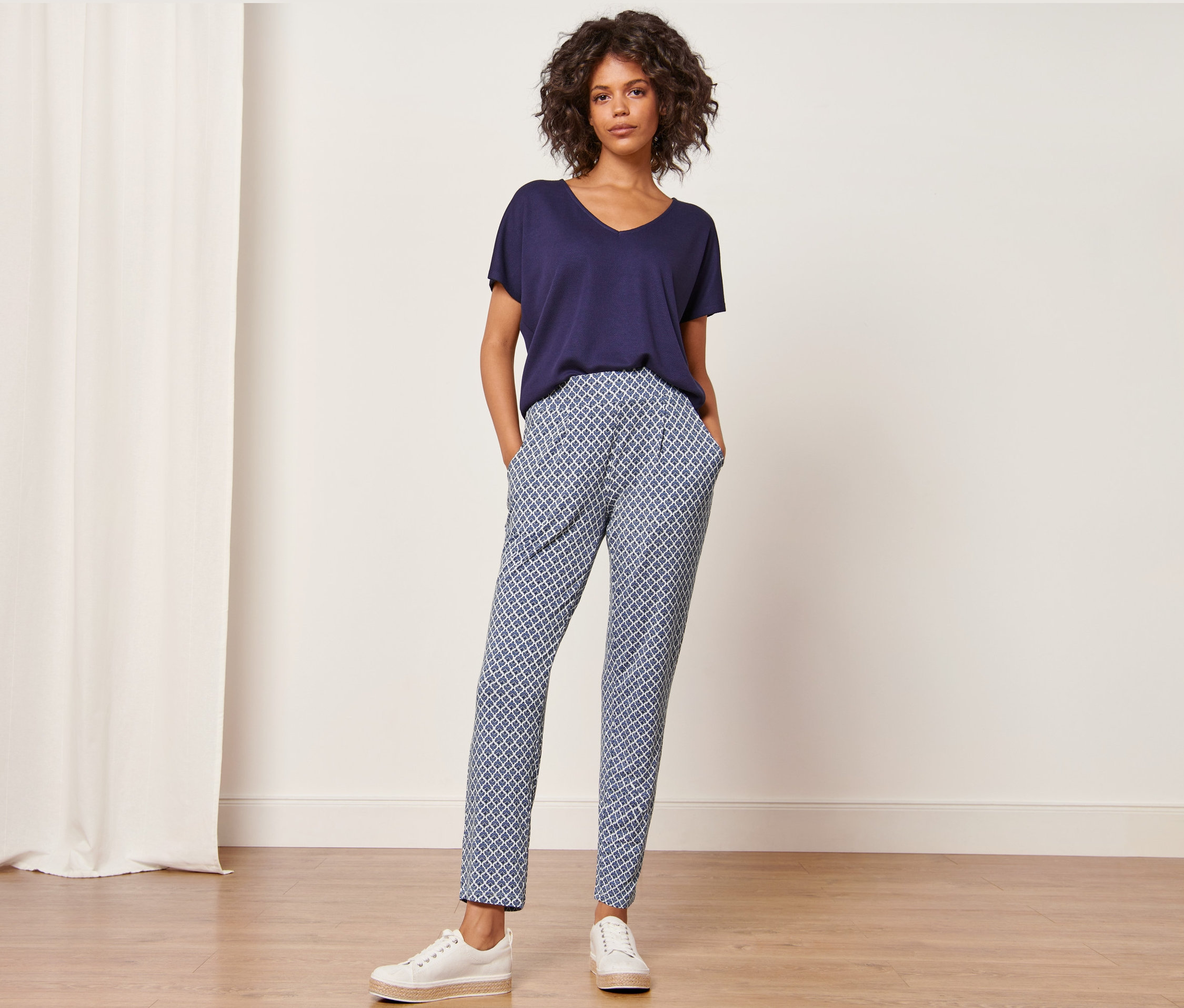 Frau steht mit Händen in den Taschen der bedruckten Jerseyhose.