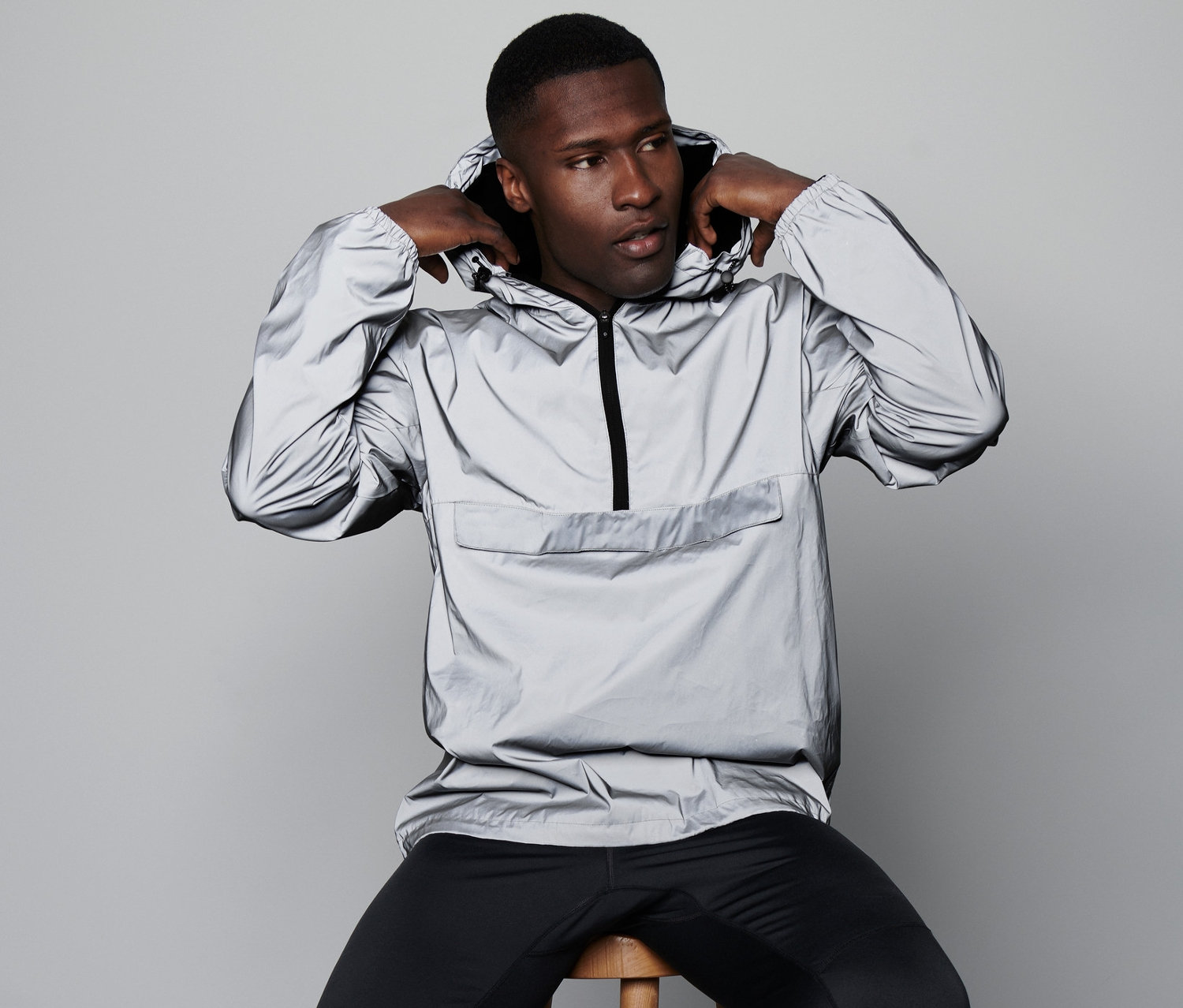 Mann sitzt auf einem Hocker und zieht einen reflektierenden Windbreaker an.