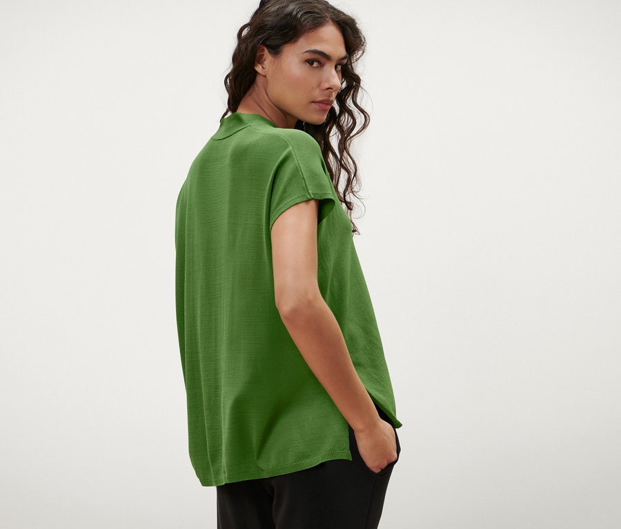 Frau blickt über die Schulter und trägt einen kurzärmligen Cardigan in Grün.