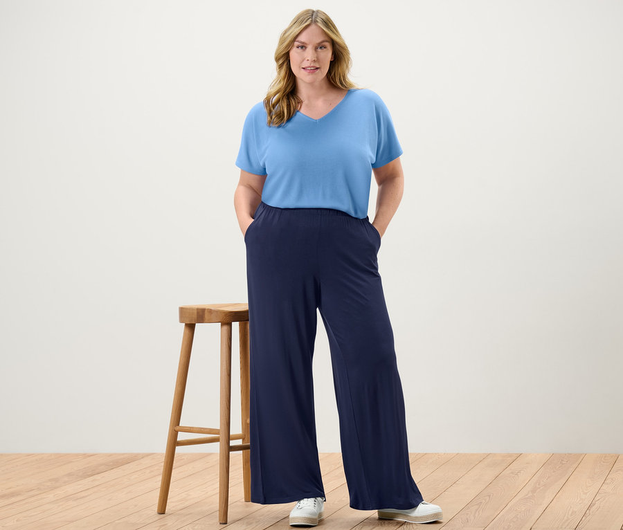 Eine Frau steht mit den Händen in den Taschen ihrer dunkelblauen Palazzohose und einem hellblauen, strukturierten Shirt.