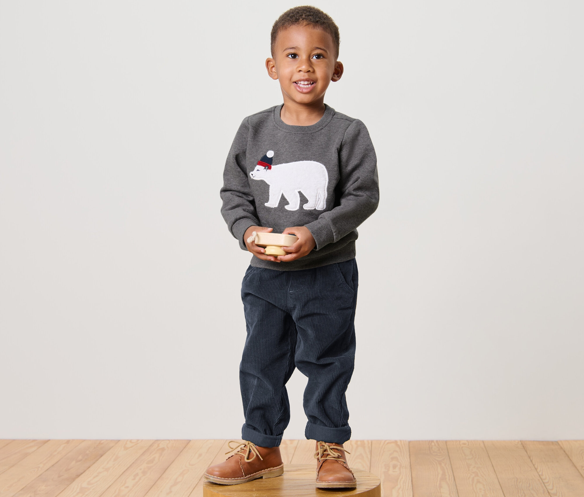 Junge steht und hält ein Holzspielzeug. Er trägt einen Kinder-Sweater mit einem Eisbären.
