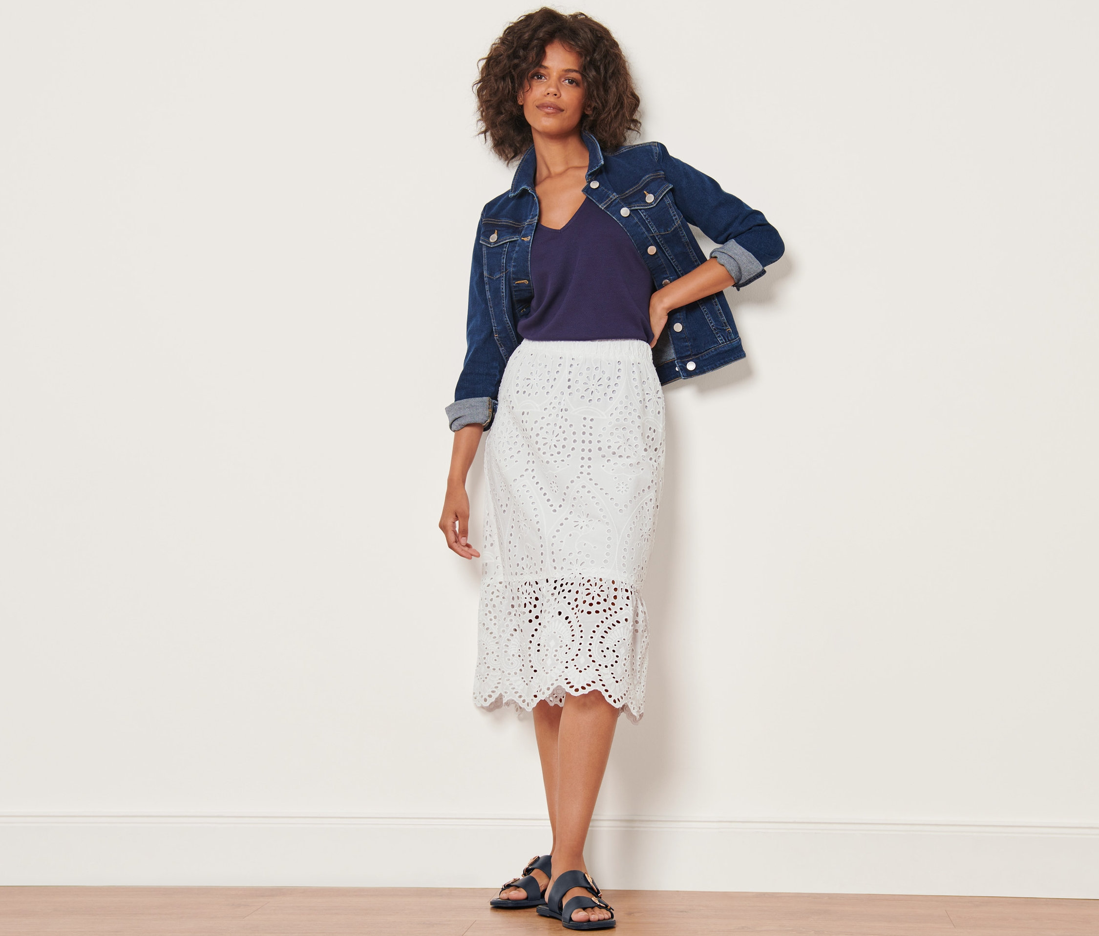 Frau posiert in Jeansjacke und weissem Rock mit Lochstickerei.