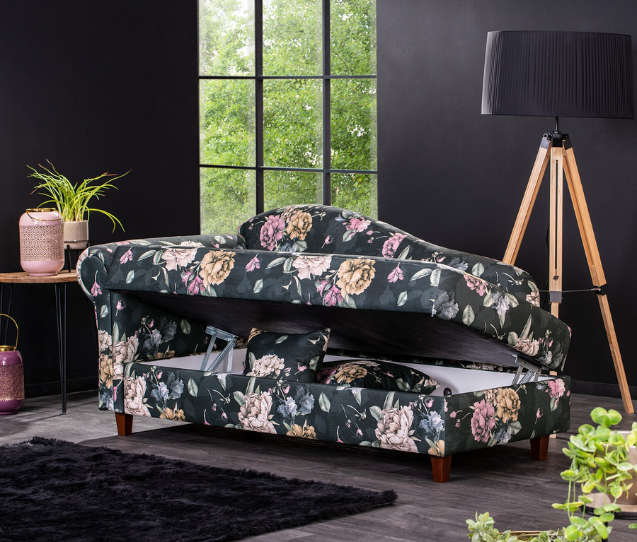 Die Polster-Recamiere »Evelyn« links mit floralem Muster und Stauraum steht in einem Wohnzimmer mit schwarzen Wänden.