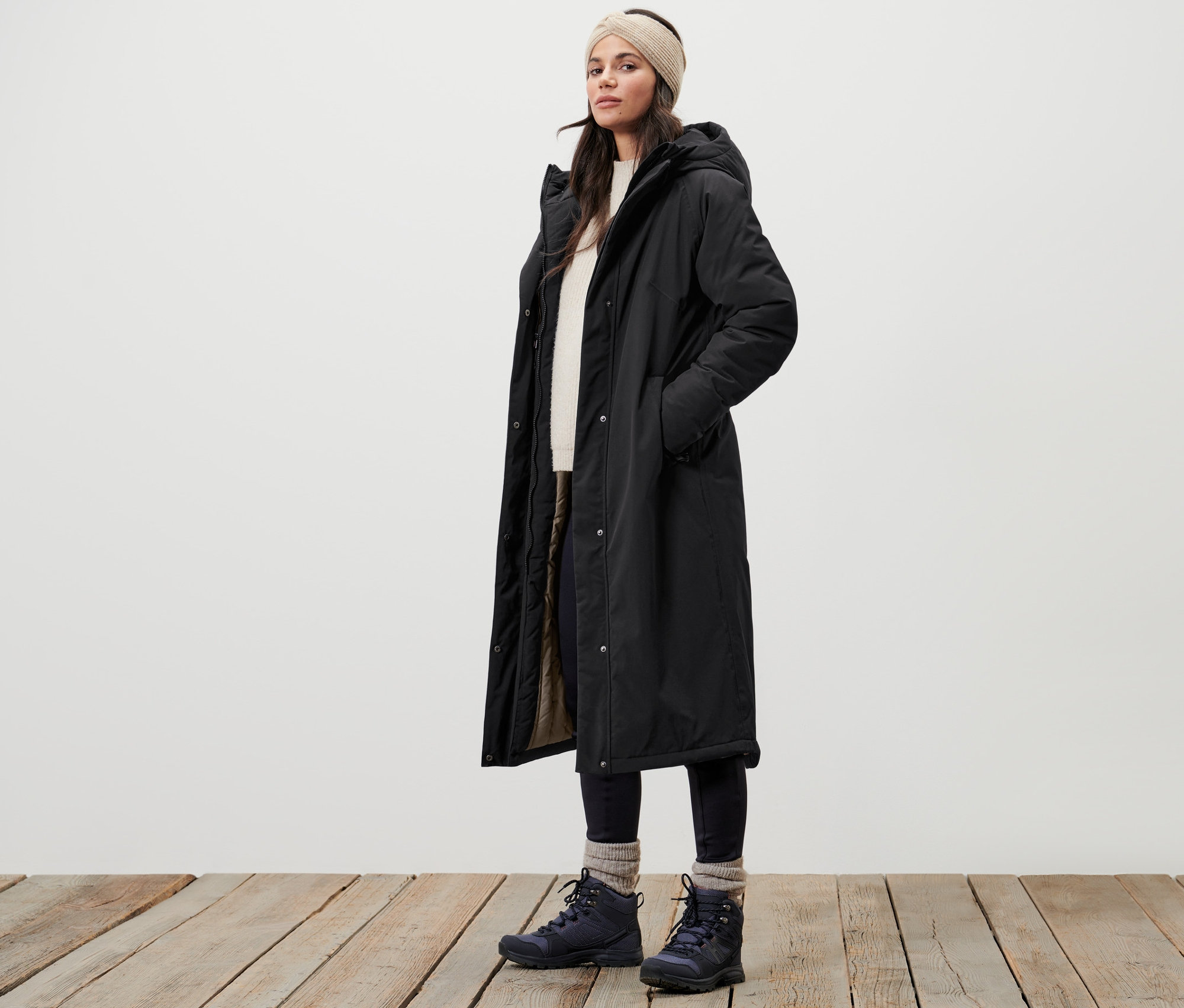 Frau steht auf Holzboden und trägt einen extralangen Thermomantel.