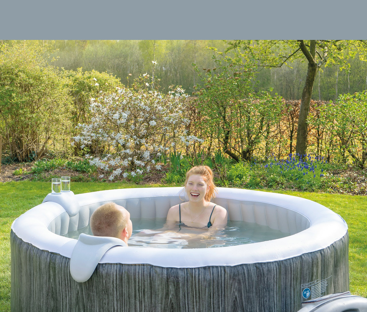 Zwei Personen sitzen im EXIT Wood Deluxe Whirlpool für 4 Personen im Garten.