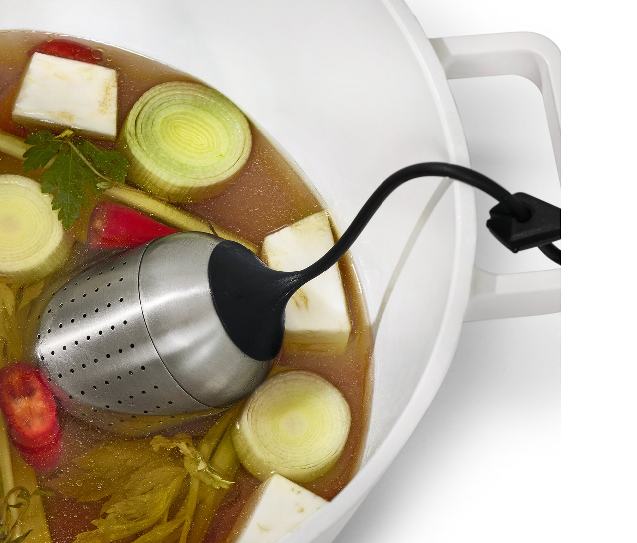 Eine Gewürzkugel hängt in einem Topf mit Brühe und Gemüse.