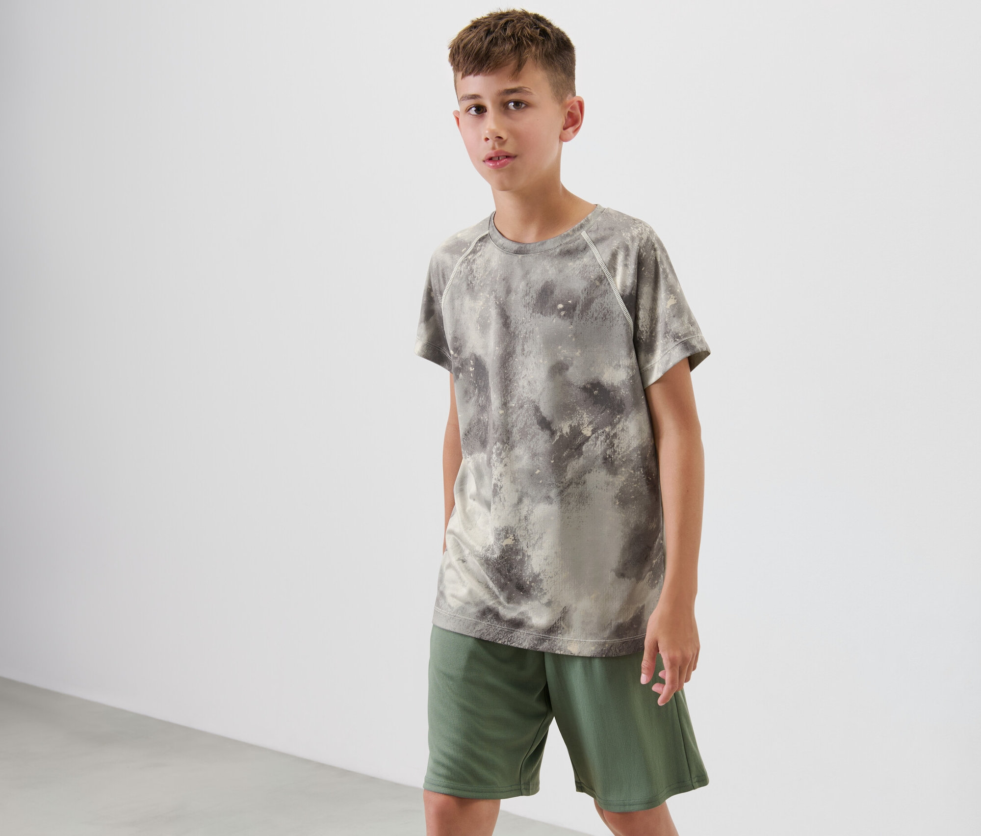 Ein Junge steht und trägt ein grünes Kinder-Sportshirt mit Alloverprint.