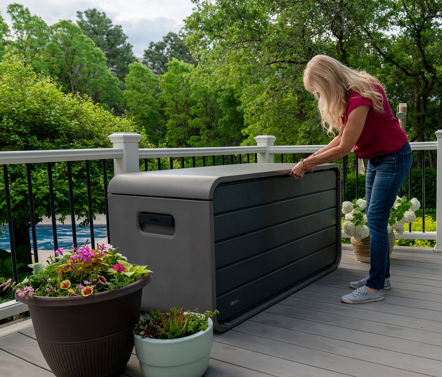 Blonde Frau öffnet graubraune Aufbewahrungsbox (625 l) auf Terrasse.