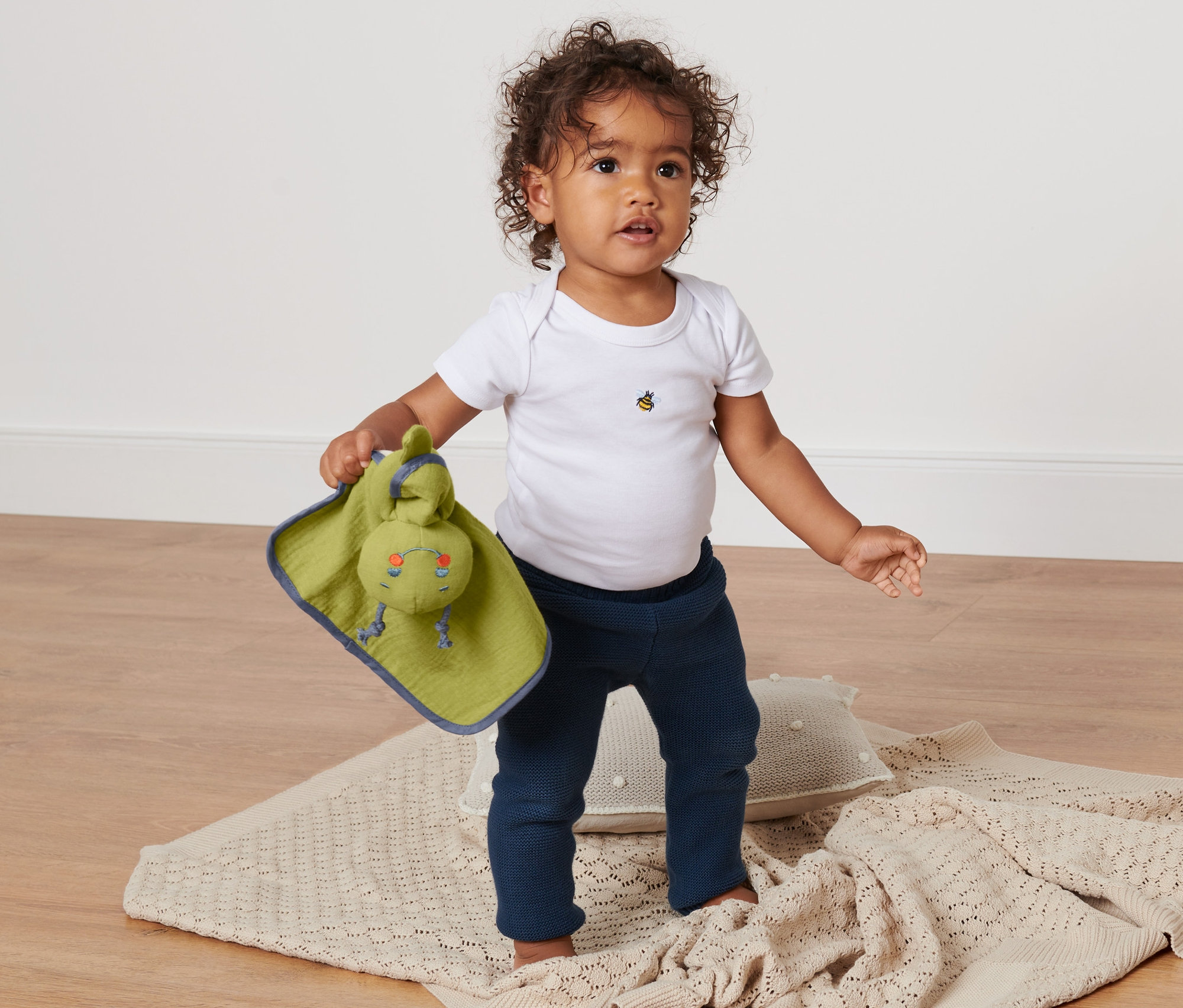 Kleinkind steht auf einer Decke und hält ein Baby-Schmusetuchtier.