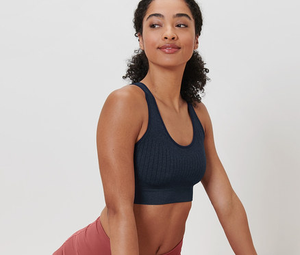 Frau in dunkelblauem Seamless-Sport-Bustier und rosafarbenen Leggings dehnt sich auf einer Matte.
