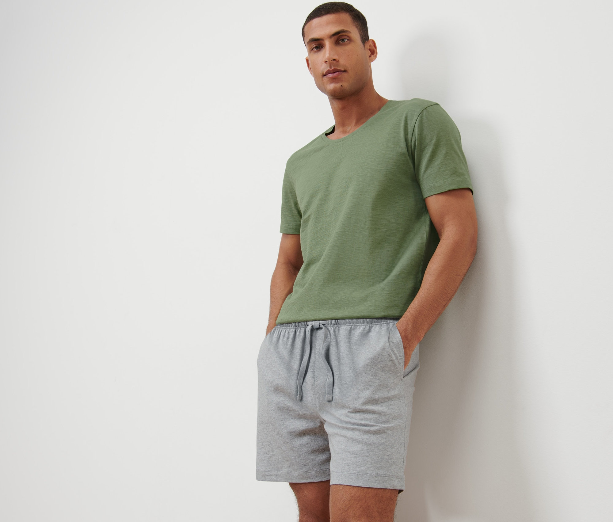 Ein Mann posiert in einem Shorty-Pyjama und einem grünen T-Shirt.