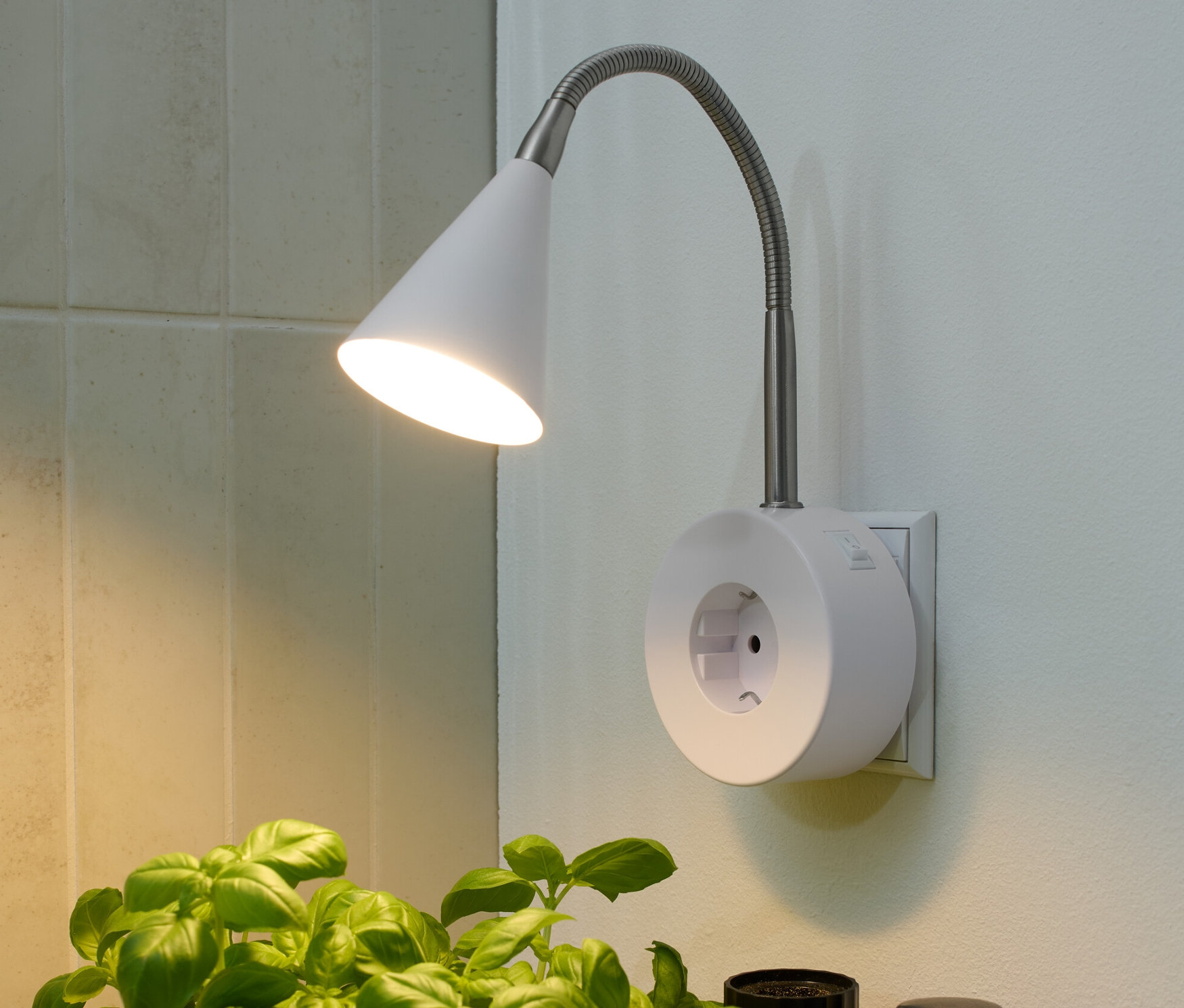 Eine schwenkbare LED-Leuchte beleuchtet Basilikum im Topf neben Pfeffer und Olivenöl.