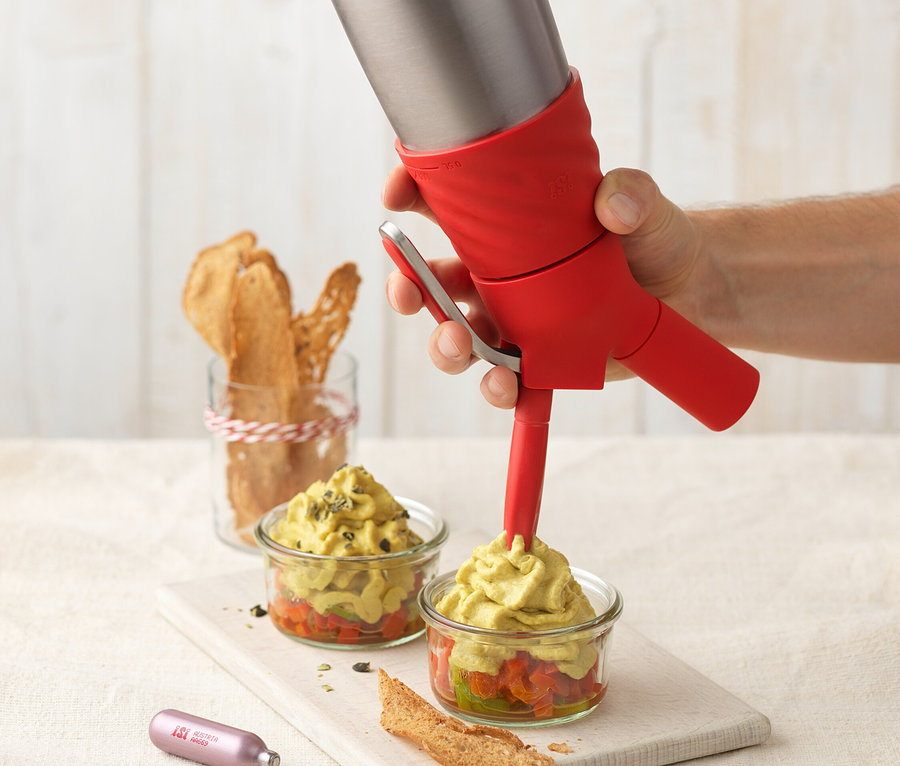 Eine Hand füllt mit einem ISI Creative Whip, 0,5 l, Avocadoschaum in zwei Gläser.