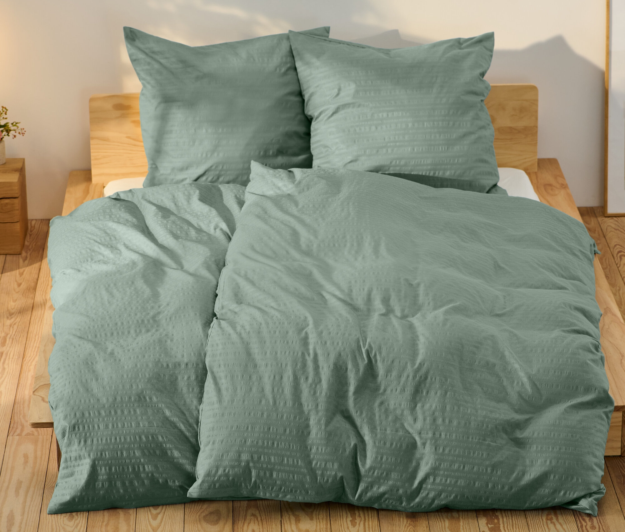 Grüne Seersucker-Bettwäsche in Normalgröße und eine in Übergröße auf einem Bett.