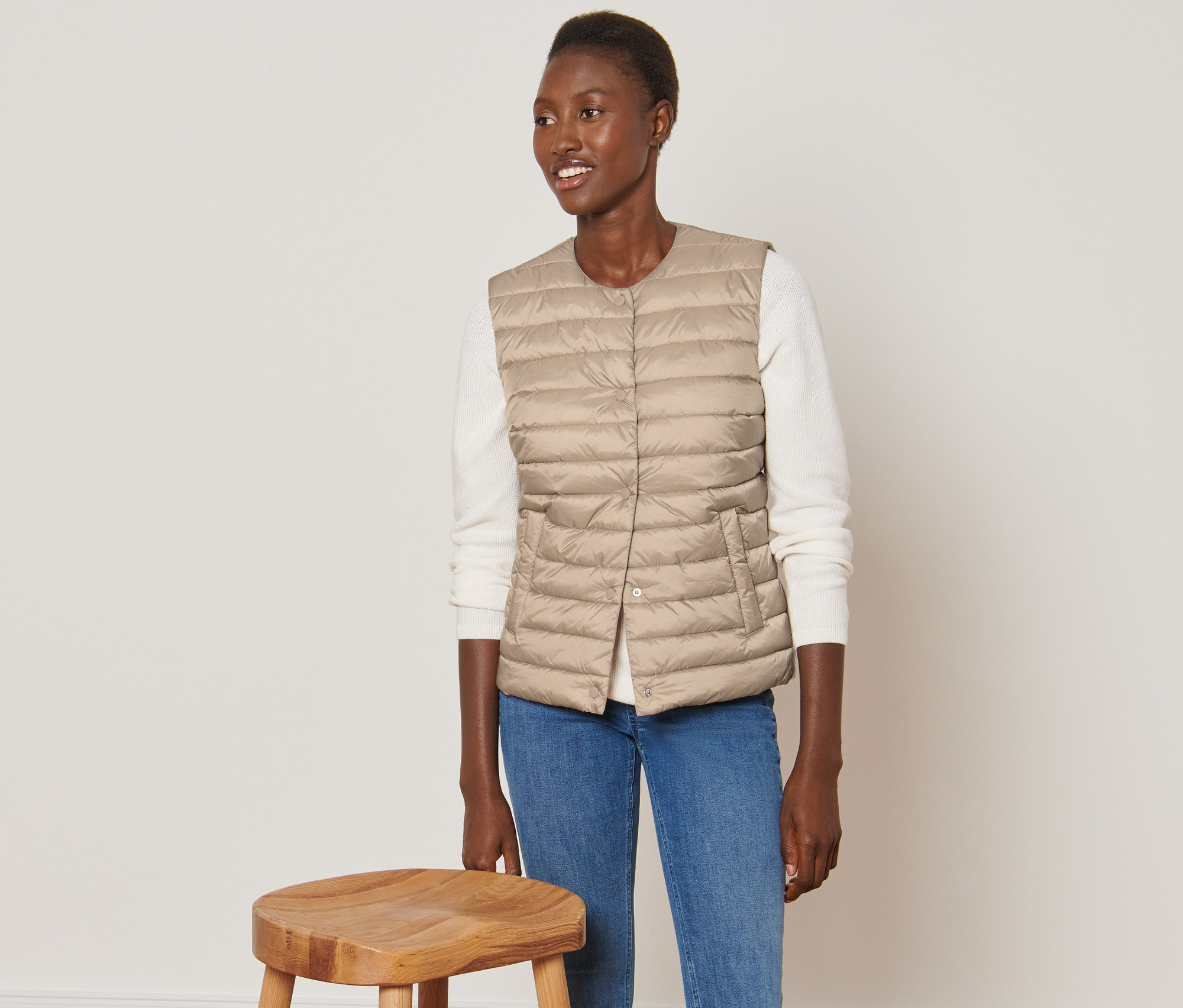 Frau trägt eine Steppweste und steht neben einem Holzhocker.