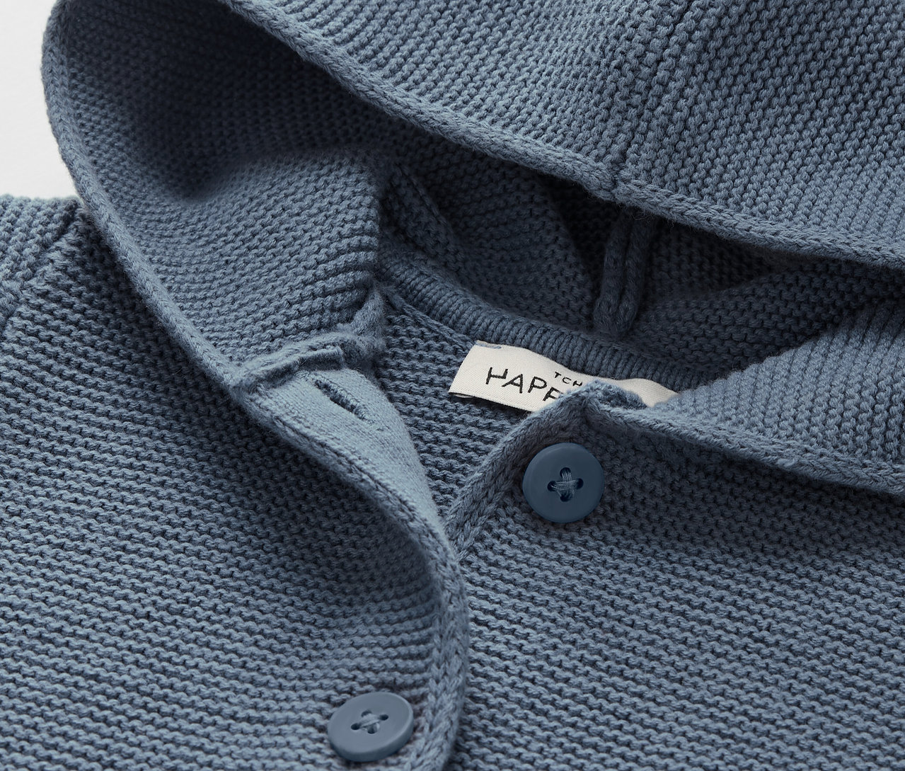 Detailaufnahme einer blauen Strickjacke mit Kapuze und Knöpfen.