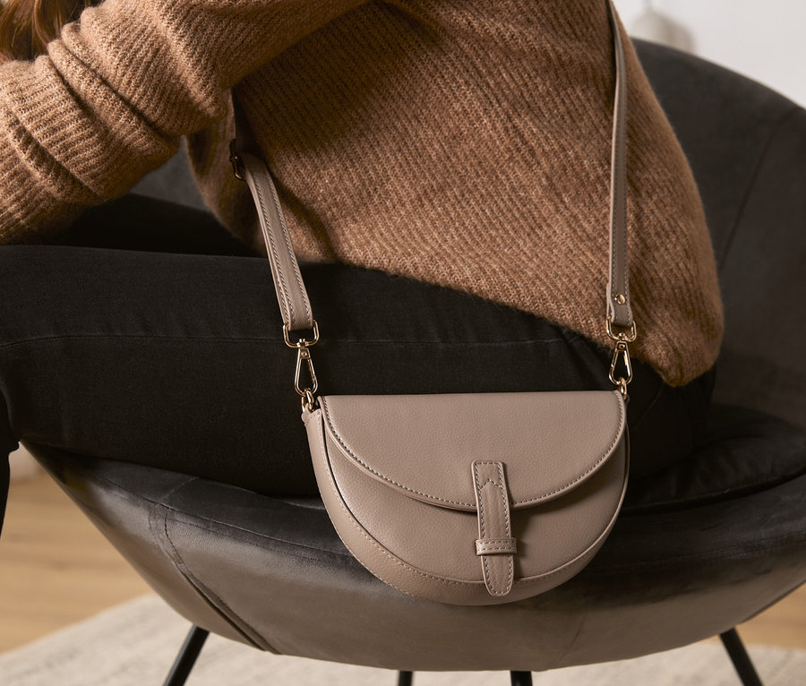 Frau sitzt im Sessel mit beiger Umhänge- und Bauchtasche.