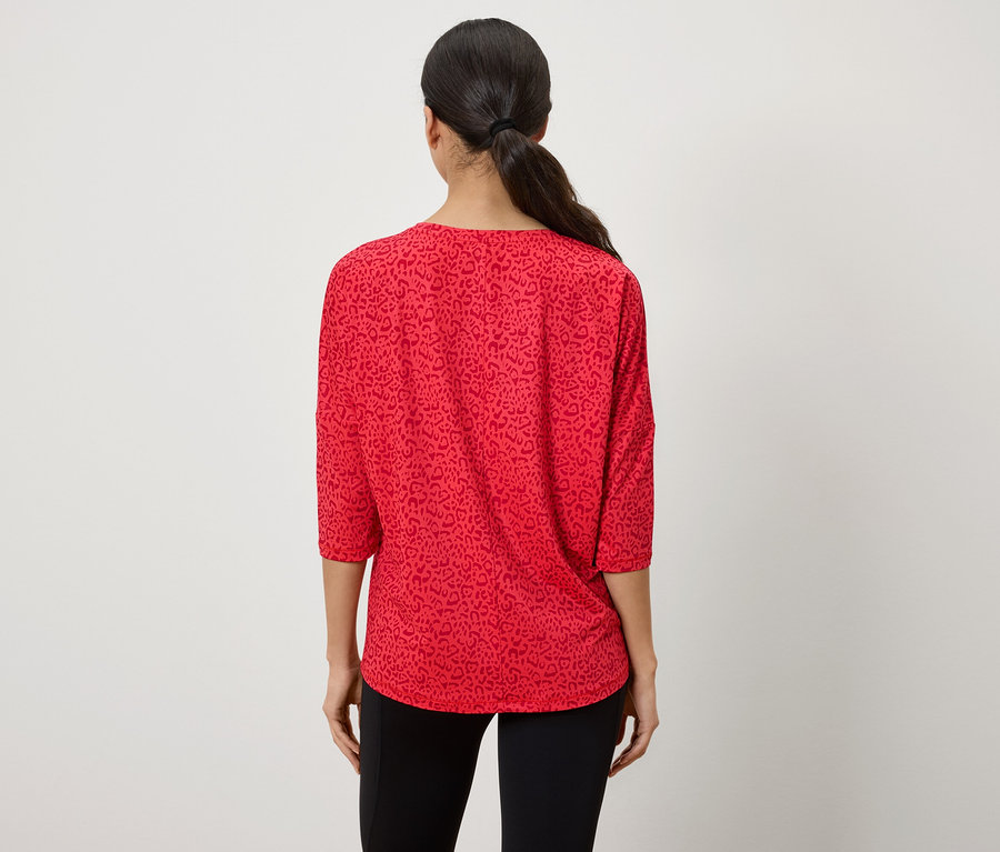 Von hinten ist eine Frau mit zu einem Pferdeschwanz zusammengebundenen Haaren zu sehen, die ein rotes Oberteil mit Dreiviertelärmeln und Tiermuster trägt.