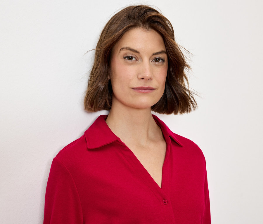 Porträt einer Frau mit braunen Haaren in einer roten Bluse mit Kragen.