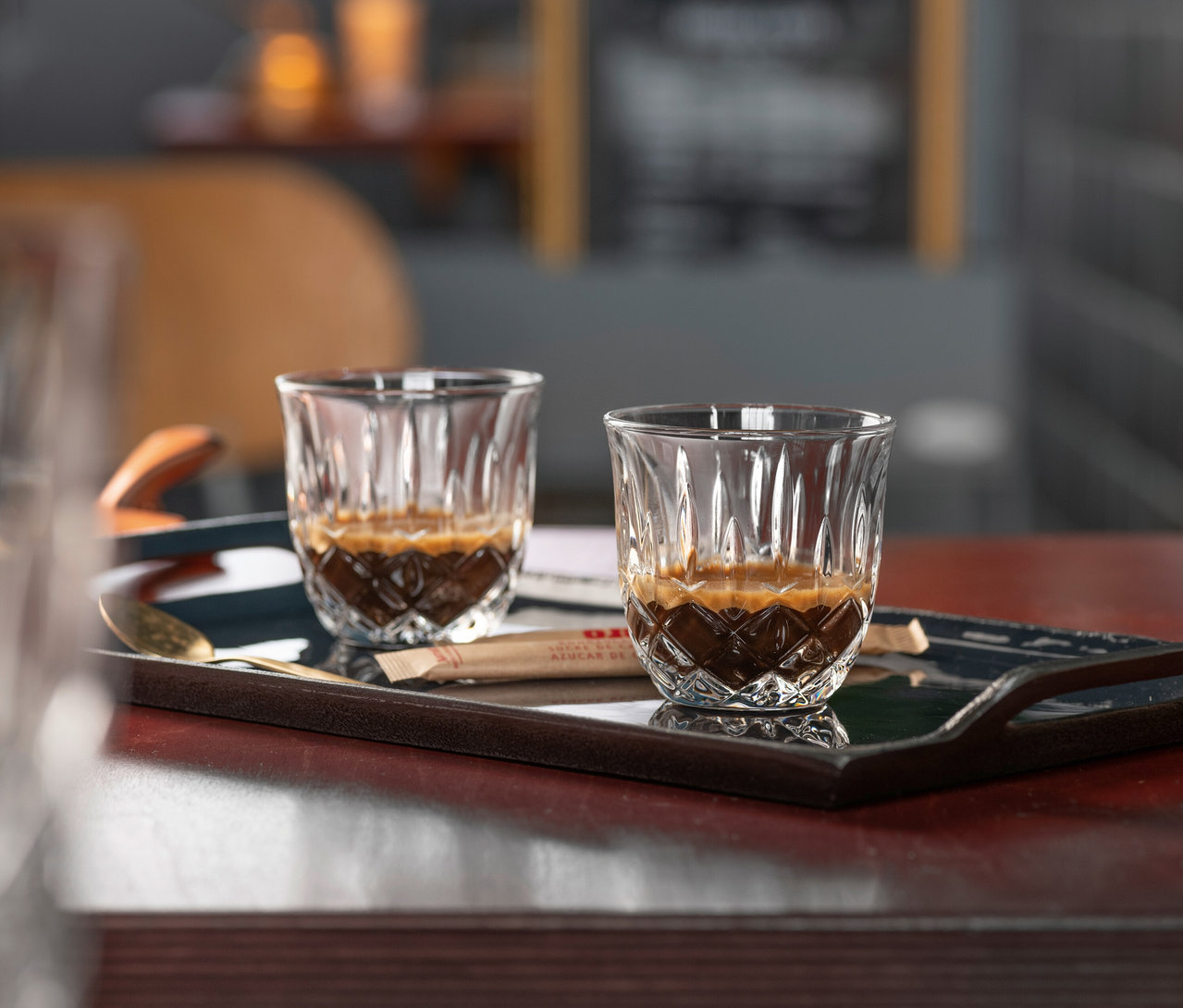 Zwei mit Espresso gefüllte Nachtmann Espressogläser »Noblesse« stehen auf einem dunklen Tablett mit Zuckersticks und einem goldenen Löffel.