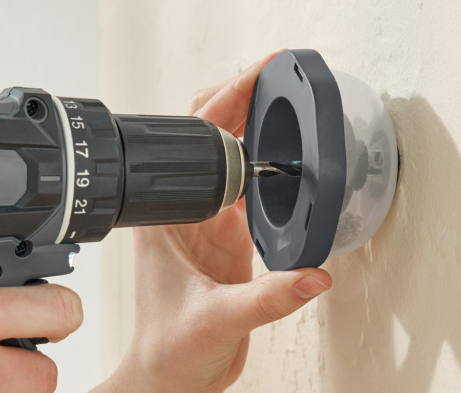 Eine Person bohrt mit einer Bohrmaschine durch einen Bohrstaubfänger in eine Wand.