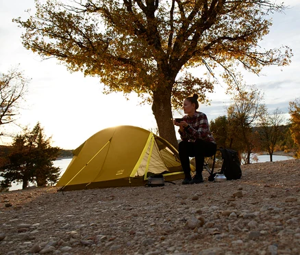 Frau sitzt vor Grand Canyon Cardova 1 Dried Tobacco Zelt und trinkt aus einer Tasse.