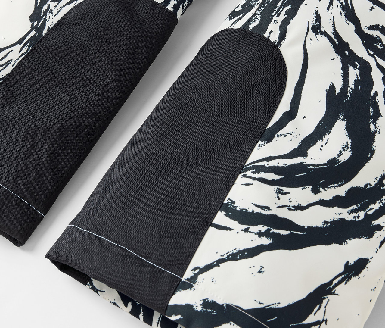 Detail einer schwarz-weißen Hose mit abstraktem Muster und schwarzen Kniepatches.