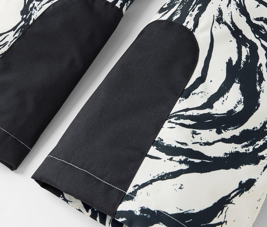 Detail einer schwarz-weißen Hose mit abstraktem Muster und schwarzen Kniepatches.