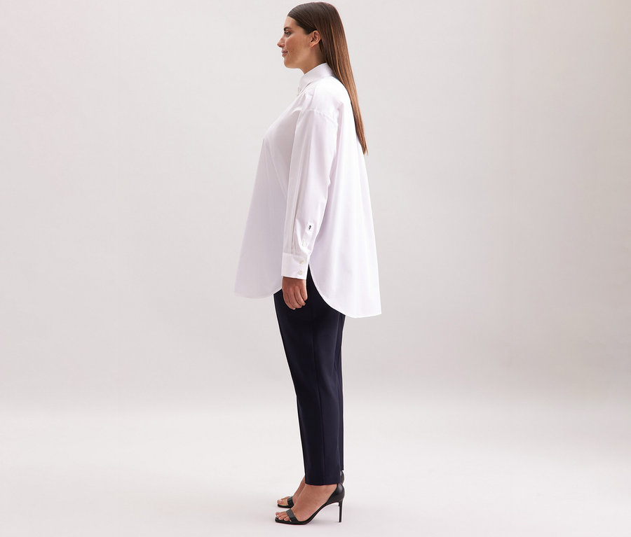 Frau trägt eine weiße Seidensticker Oversize Longbluse, dunkle Hose und schwarze High Heels.