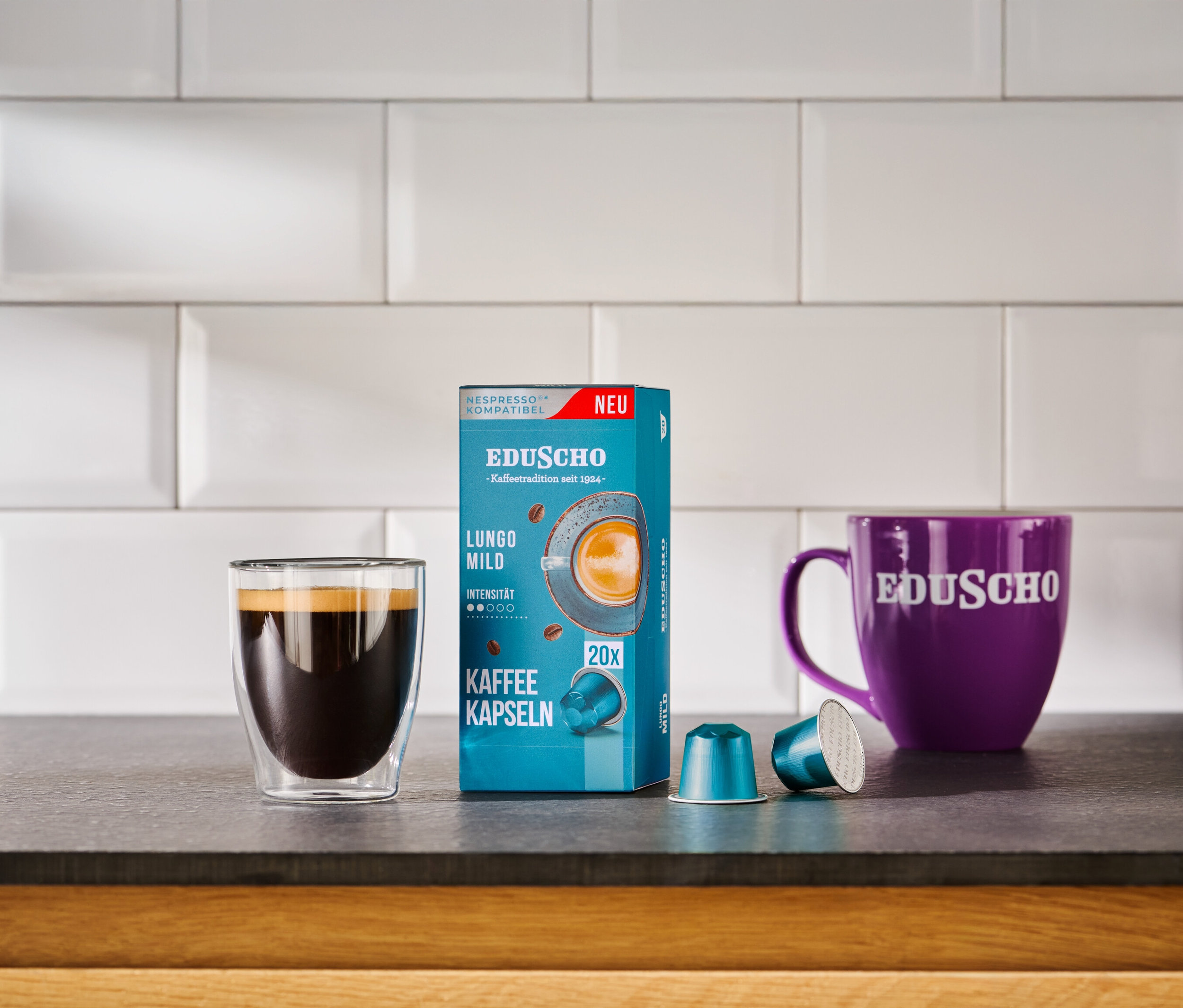 Kaffee im Glas neben Packung Eduscho Lungo Mild Kaffeekapseln und lila Eduscho Tasse.