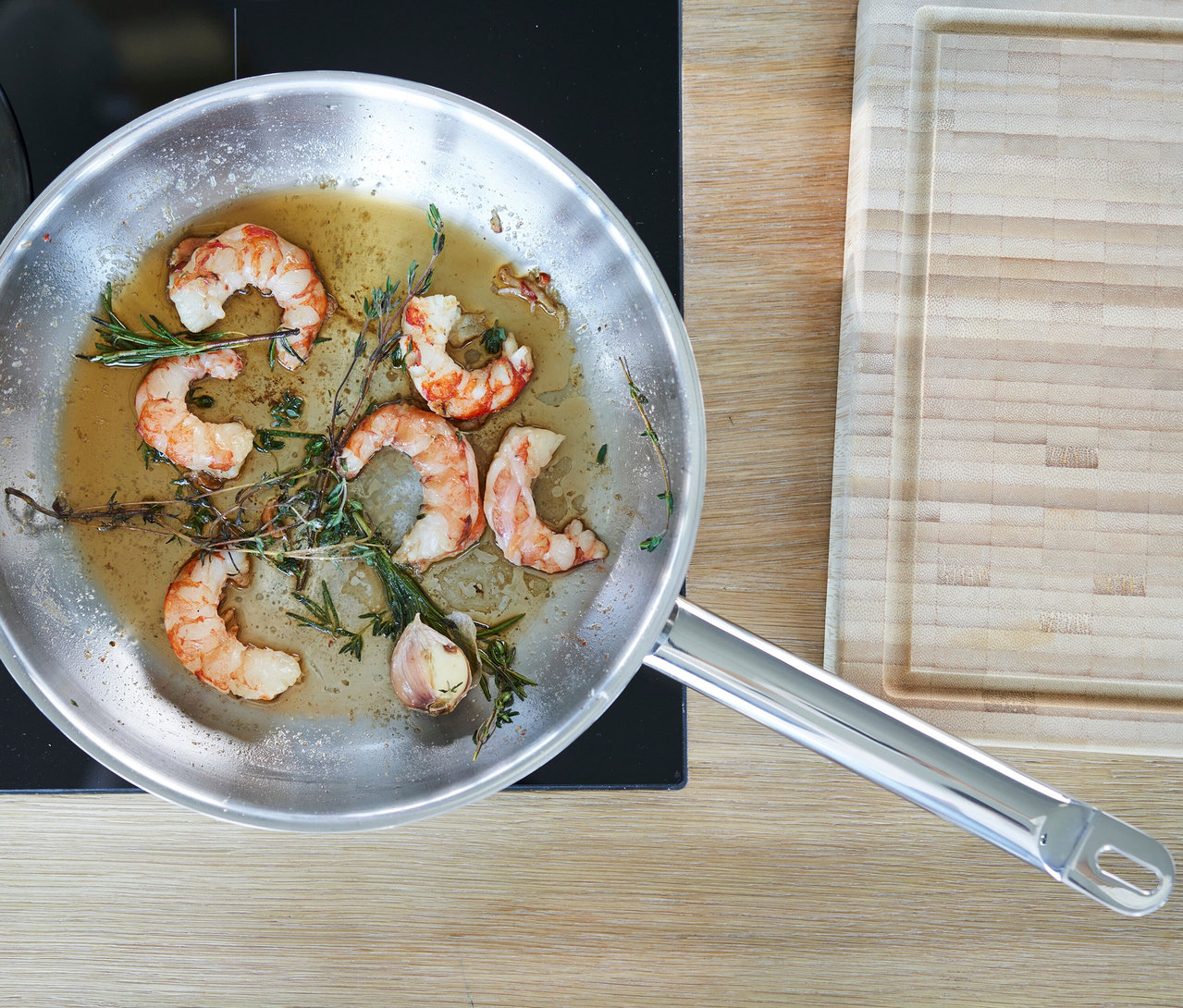 Gekochte Garnelen mit Kräutern und Knoblauch in einer silbernen Zwilling PRO Edelstahlpfanne (ca. 24 cm) auf einem Herd.