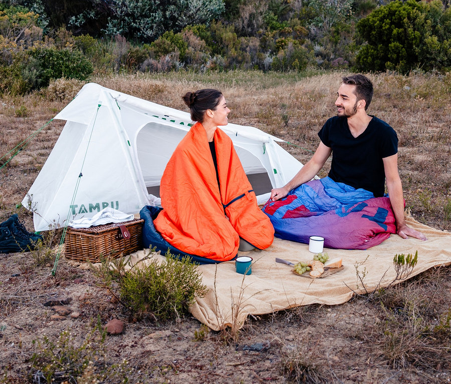 Ein Mann und eine Frau sitzen vor einem Tambu 2-Personen-Trekkingzelt »SURAN 2«.