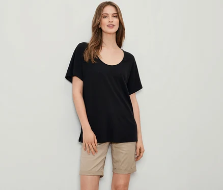 Eine Frau trägt ein schwarzes Shirt aus Leinenmix und eine beige Shorts.