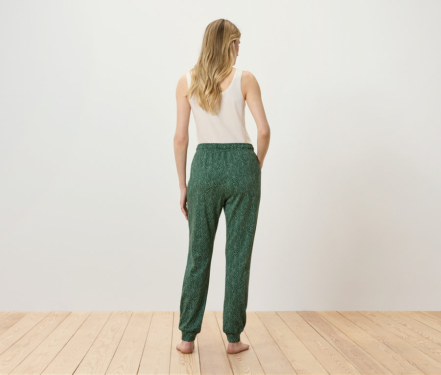 Frau mit Trägerhemd und grün gemusterter Hose steht mit dem Rücken zur Kamera.