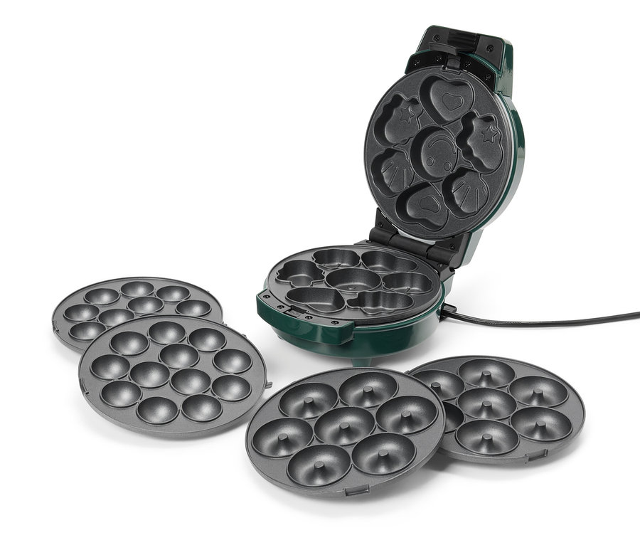 Ein grüner Donut-Maker ist geöffnet und hat verschiedene Formen, darunter ein Herz, ein Stern und ein Smiley. Zum Maker gehören vier graue Donutbleche.
