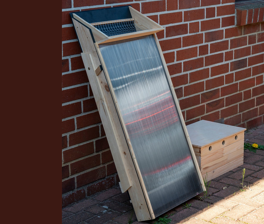 Ein Solar-Dörrschrank aus Holz lehnt an einer Ziegelwand.