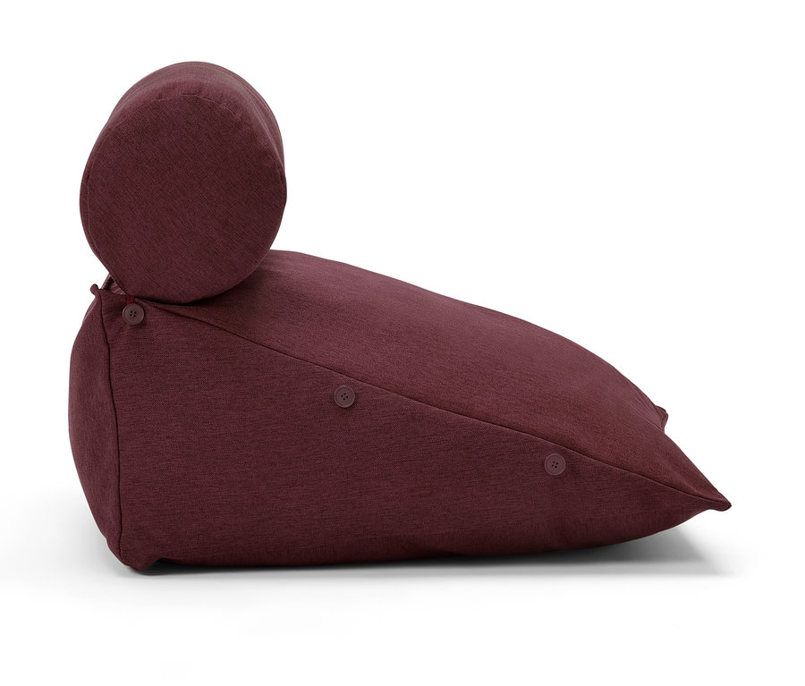 Ein weinrotes Kissen mit zylindrischer Kopfstütze und dekorativen Knöpfen.
