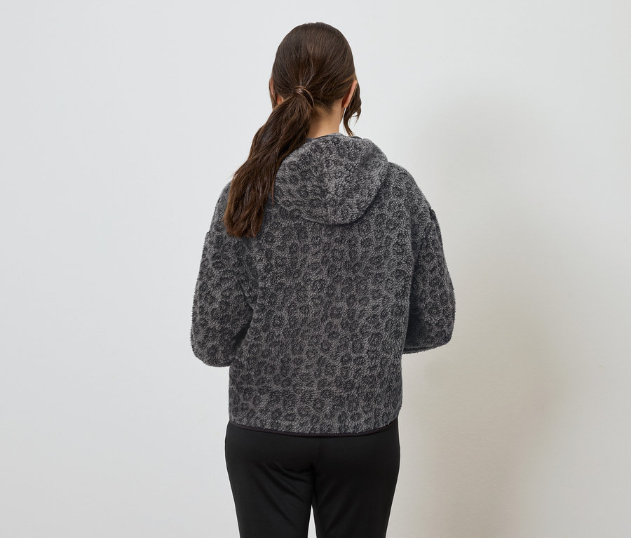 Frau mit dem Rücken zur Kamera trägt einen grauen Hoodie mit Tiermuster und eine schwarze Hose.