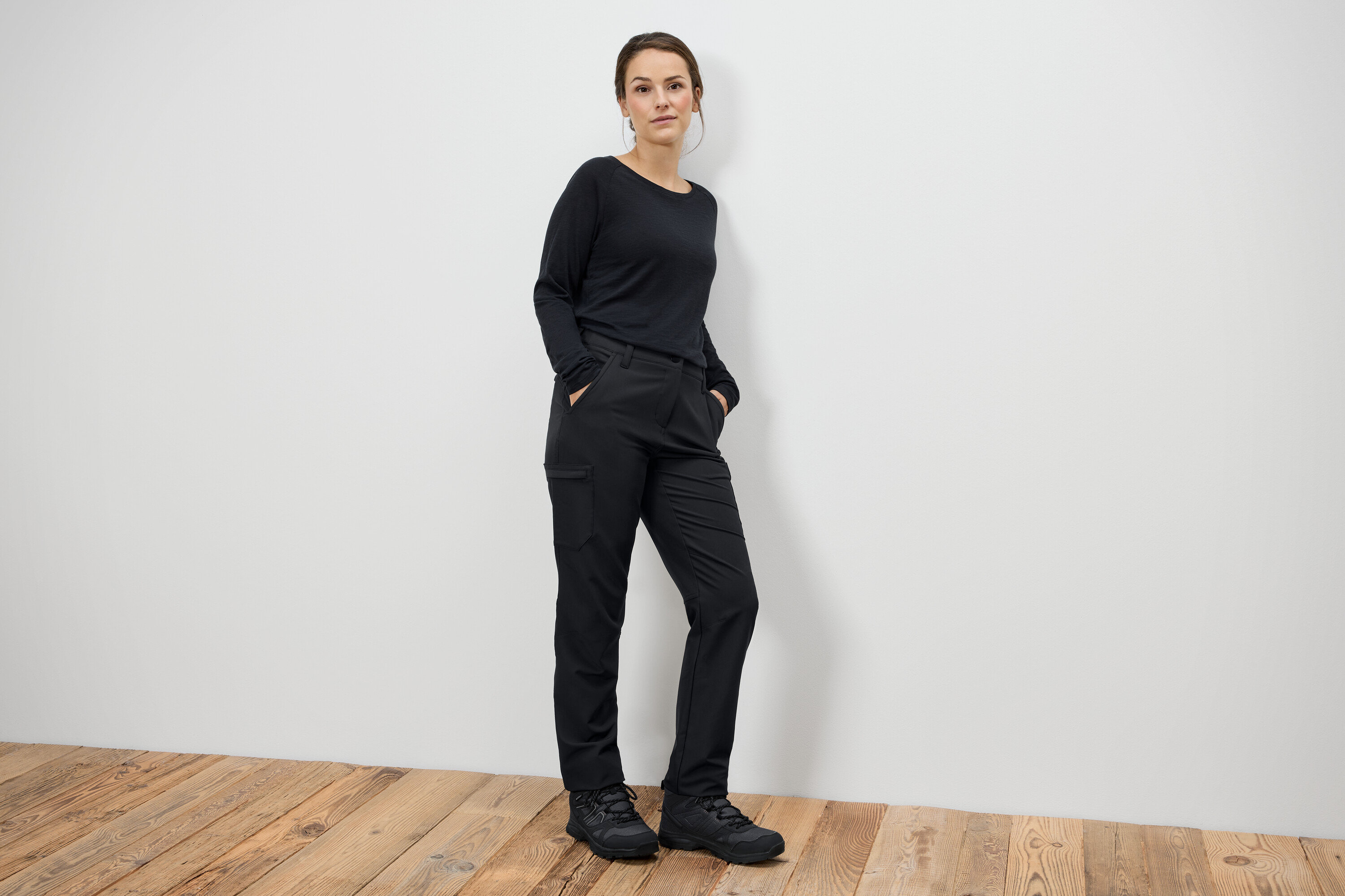 Frau steht mit Händen in den Taschen in schwarzen Hosen und schwarzen Stiefeln.