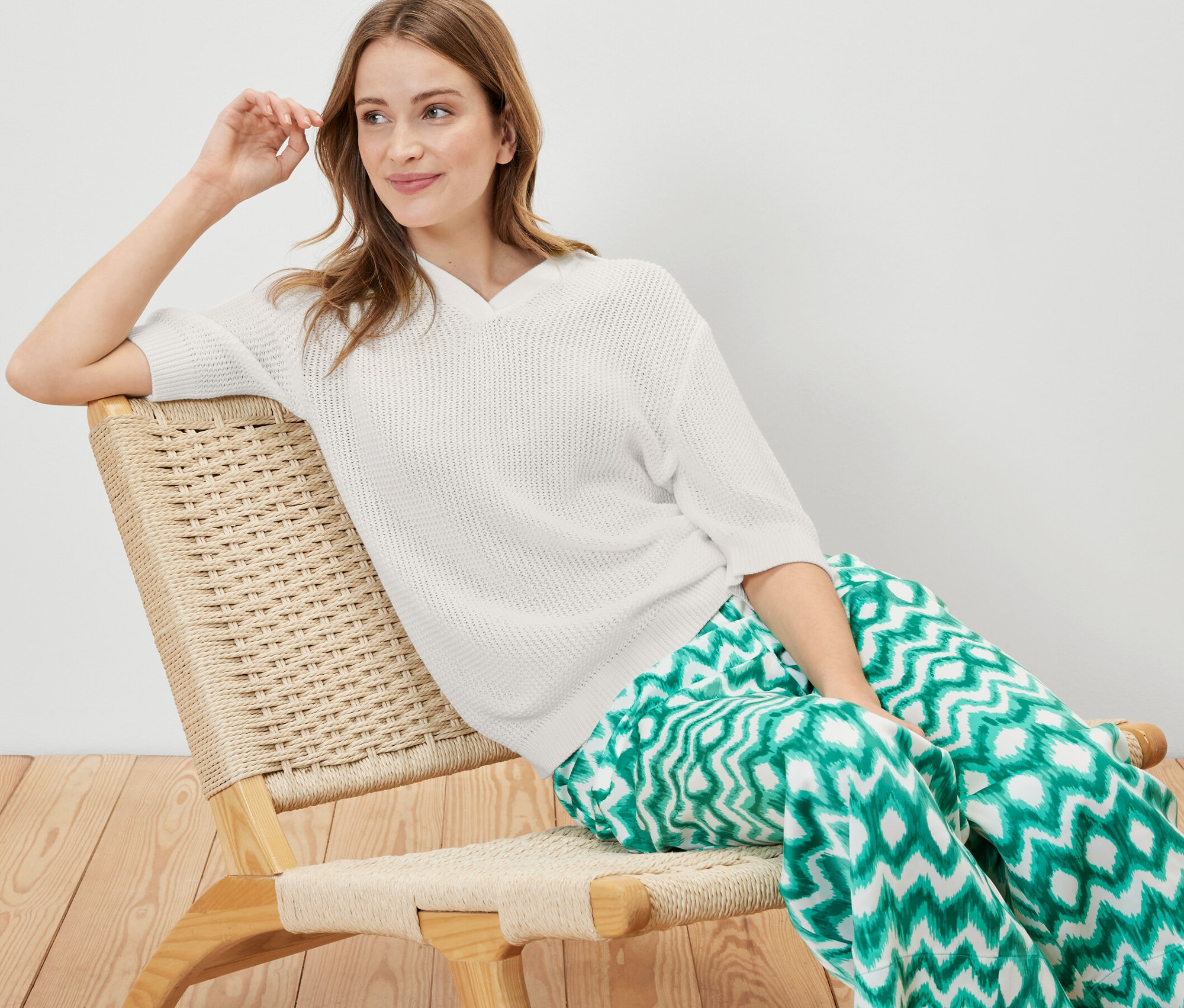 Frau sitzt im Sessel und trägt einen sommerlichen Strickpullover.