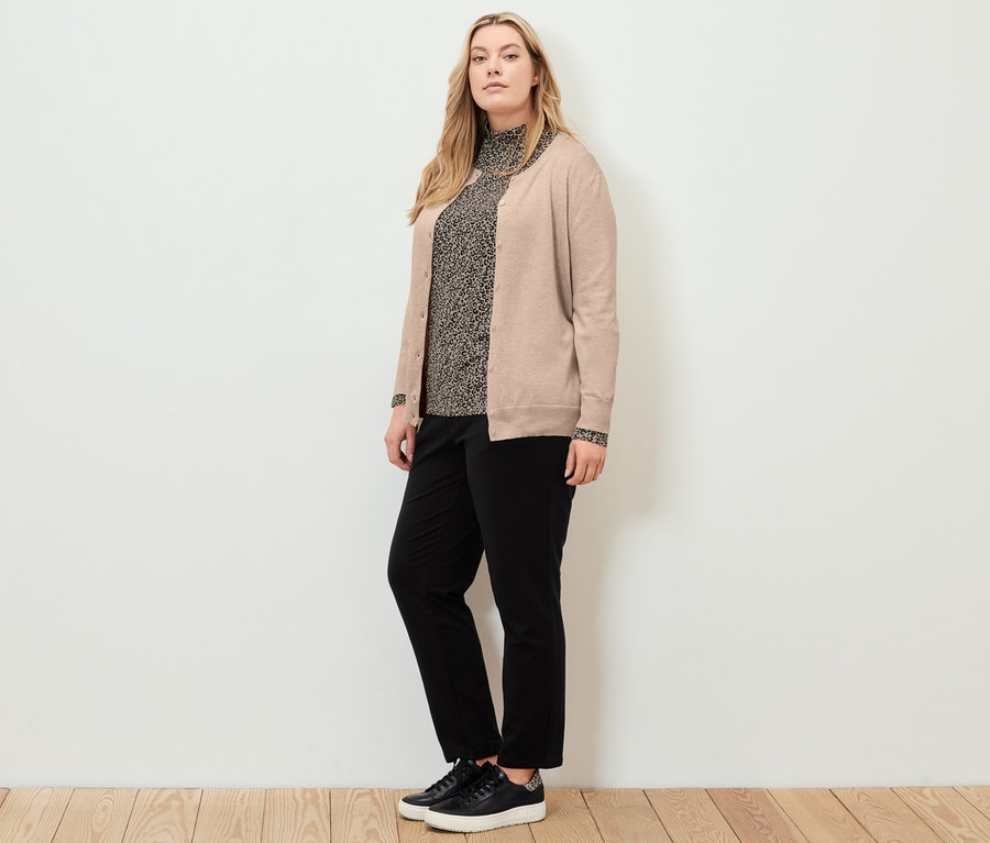 Frau posiert mit bedrucktem Blusenshirt mit Stehkragen, schwarzen Joggpants und Feinstrick-Cardigan.