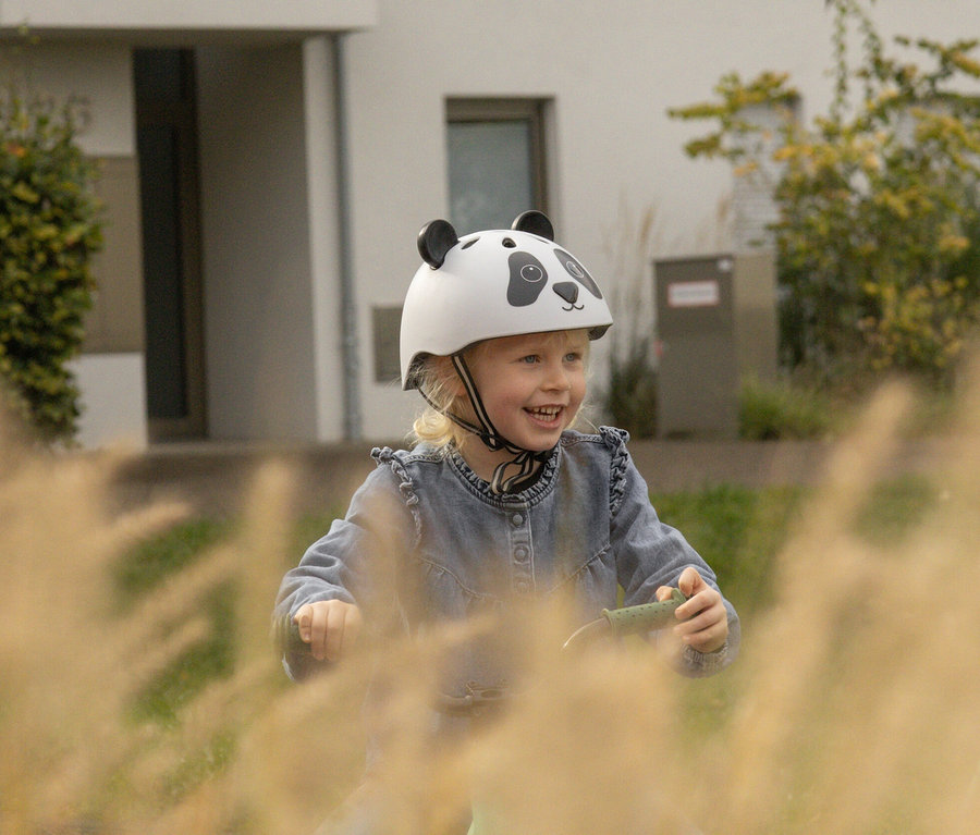 Blondes Mädchen mit HUDORA Kinderhelm »Pandy«, 44–47 lächelt und fährt Laufrad.