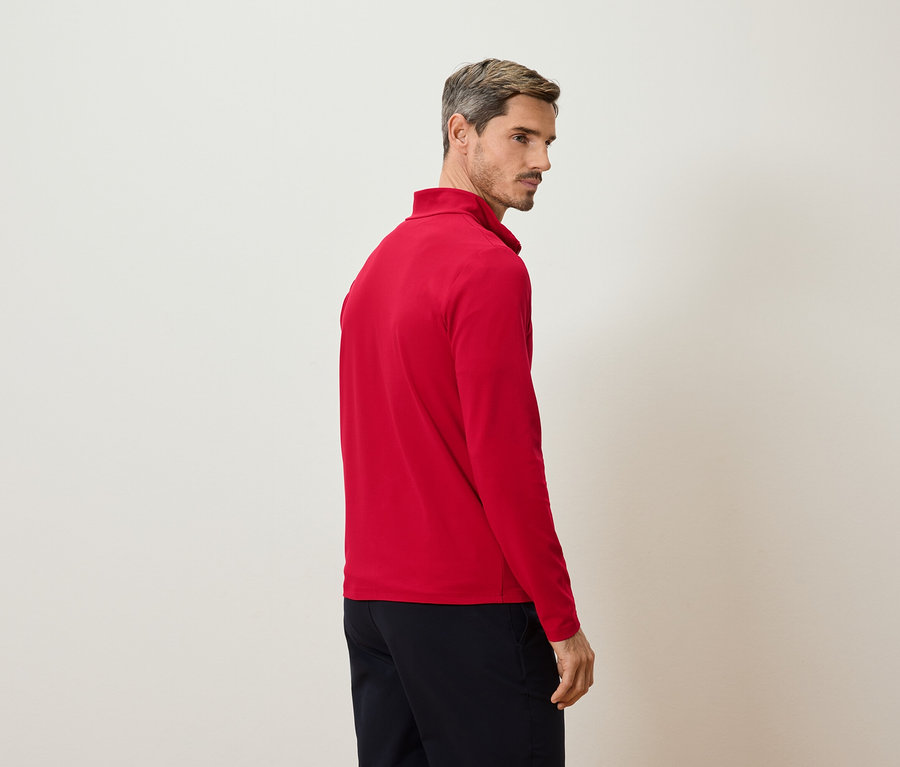 Mann von der Seite, trägt rotes Langarmshirt und dunkle Hose vor hellem Hintergrund.