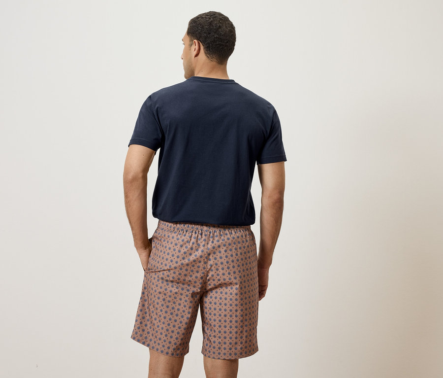 Mann von hinten in marineblauem T-Shirt und gemusterten Shorts.