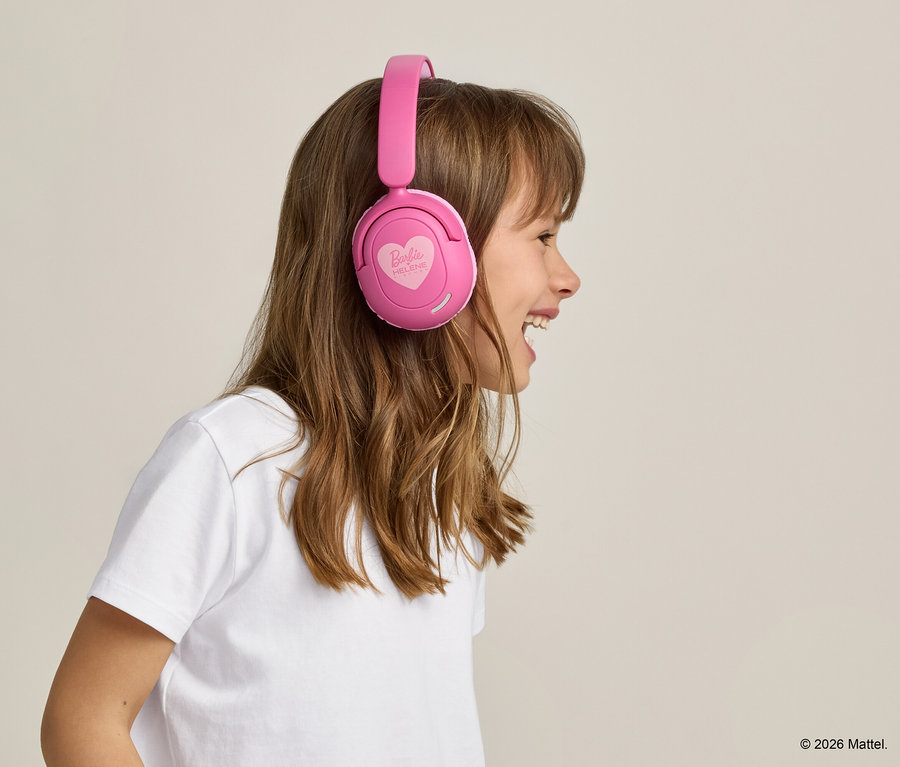 Profilansicht eines lachenden Mädchens mit langen braunen Haaren, das ein weißes T-Shirt und rosa Barbie-Kopfhörer trägt.